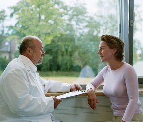 Man in white coat talks to woman.